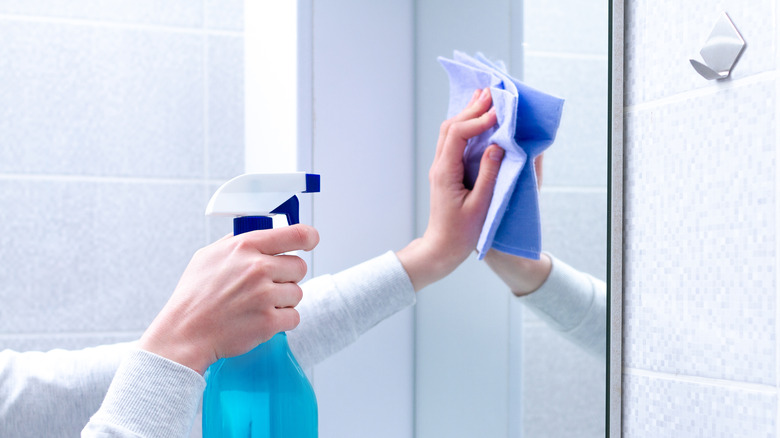 cleaning a bathroom mirror, diy blue spray bottle and rag being used on mirror