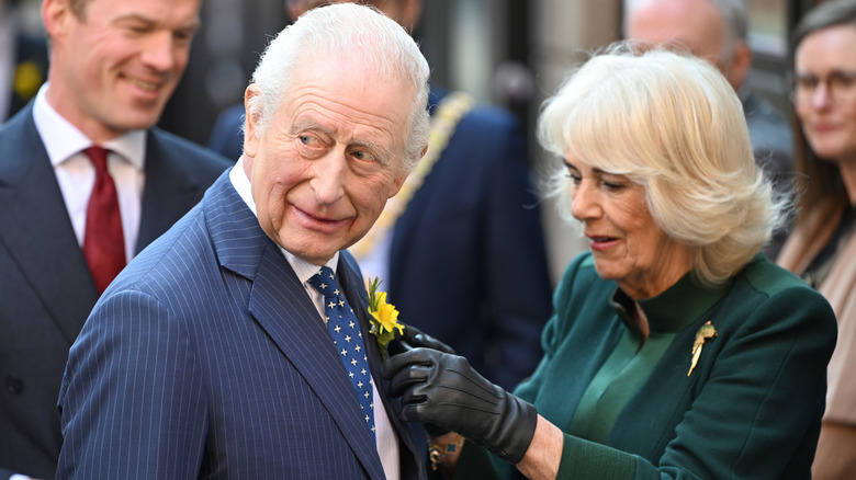 Queen Camilla adjusting a flower on King Charles' suit while onlookers watch