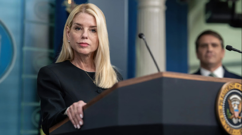 Pam Bondi addressing the media in a black outfit behind a podium