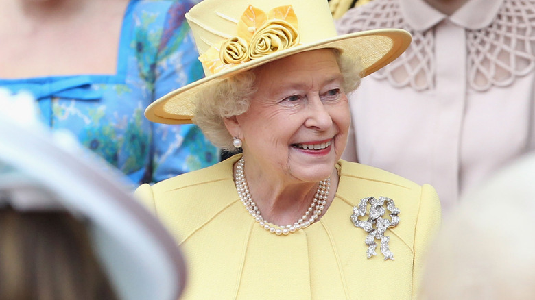 Queen Elizabeth II wears a yellow dress suit and matching hat while smiling