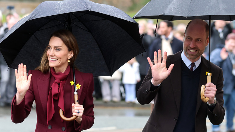 Kate Middleton and Prince William hold umbrellas as they wave at crowds