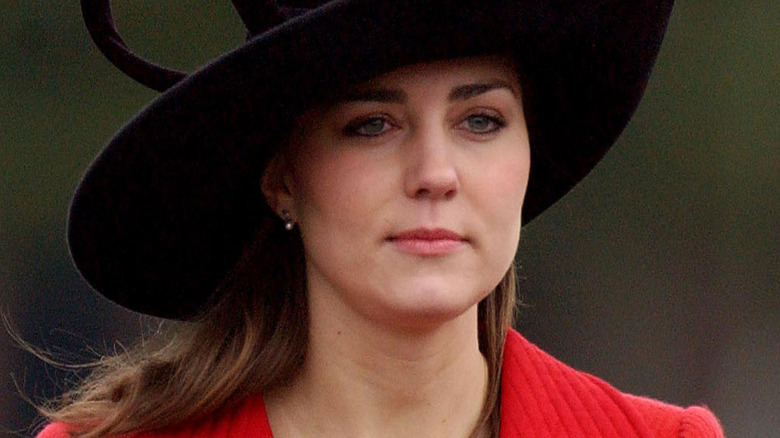 A young Kate Middleton wears a fancy black hat and a bright red coat