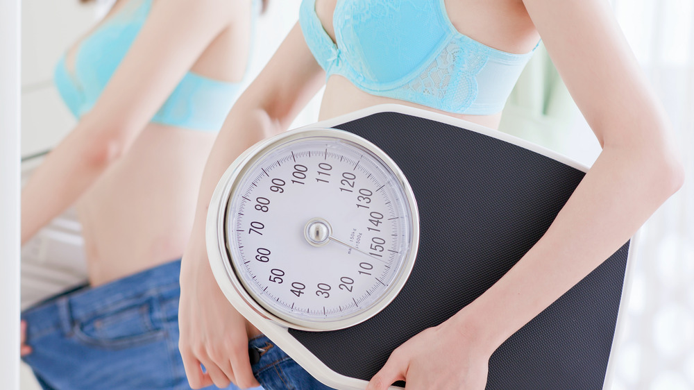 Woman in a blue bra holding a scale and showing off too big pants