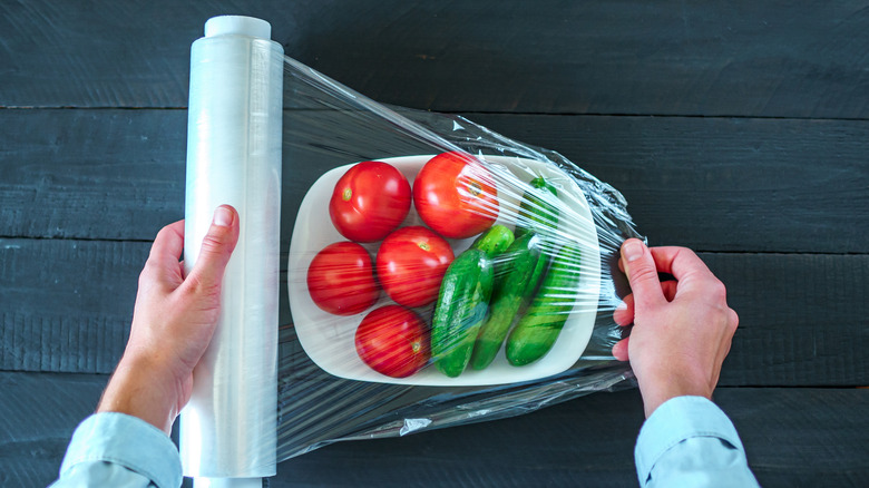 Person covering vegetables in plastic wrap