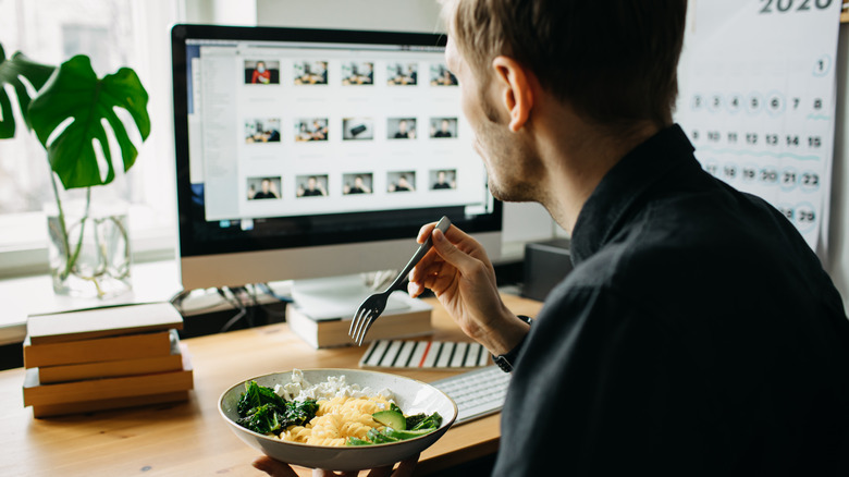 A person eats lunch while working at their desk