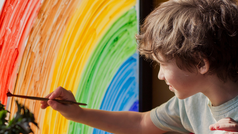 Kid painting rainbow on window