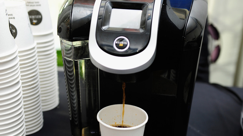 Black Keurig brewing coffee into disposable cup