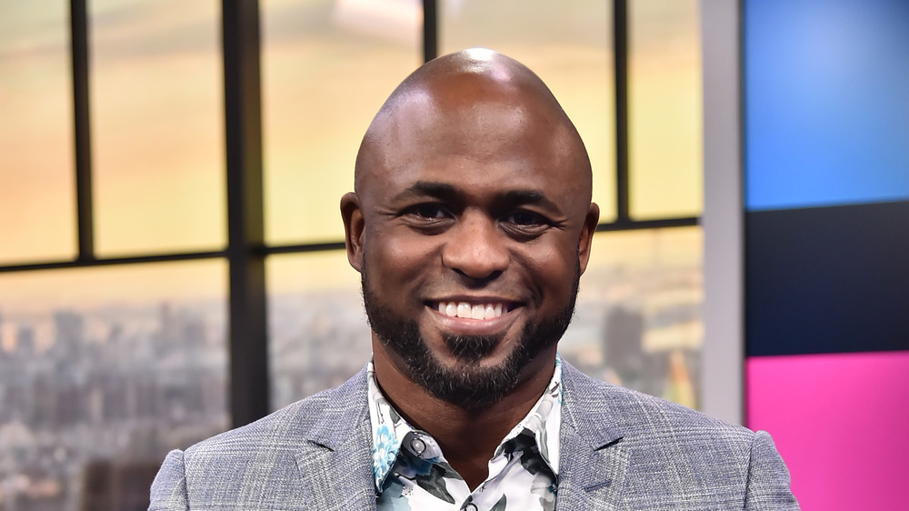 Wayne Brady smiling in a gray suit