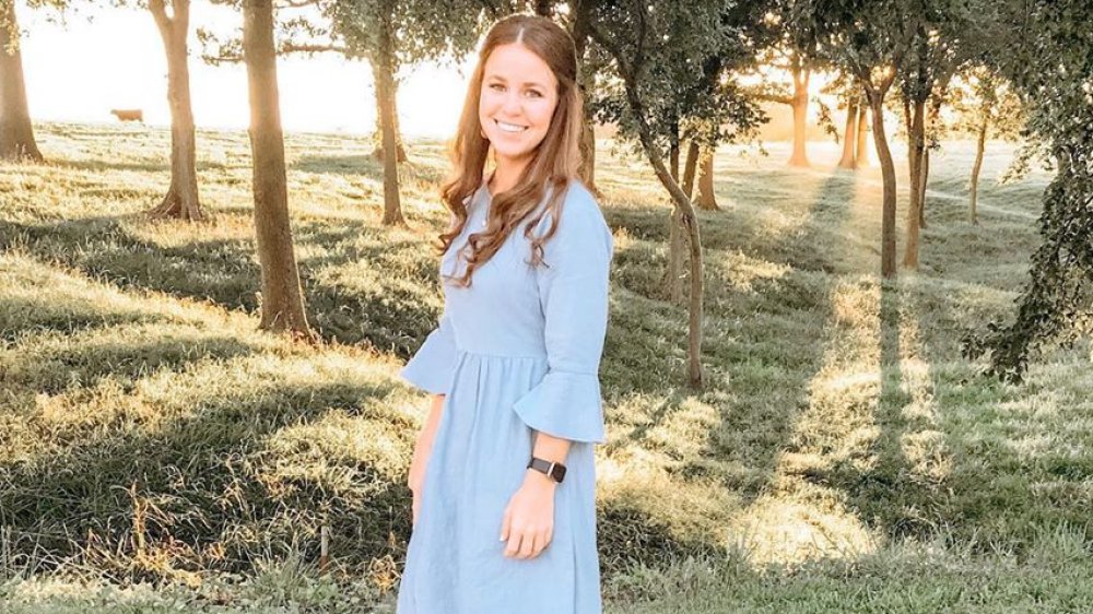 Jana Duggar smiling near trees, wearing a blue dress