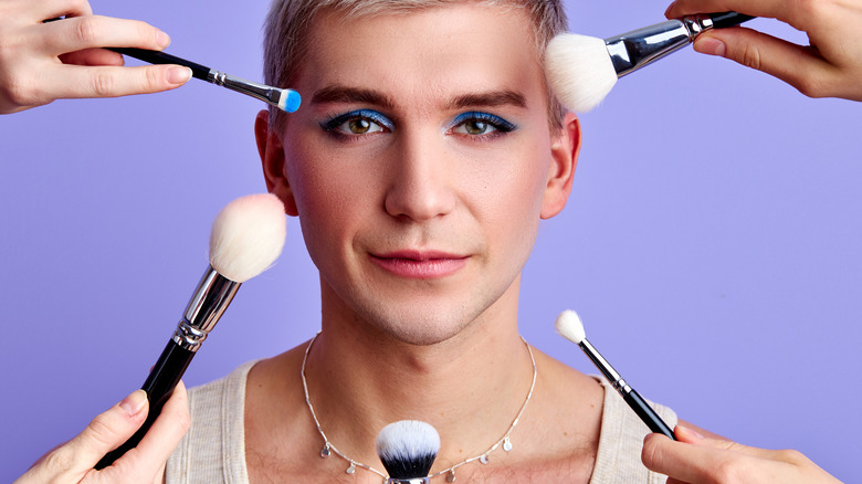 brushes applying makeup to young man's face