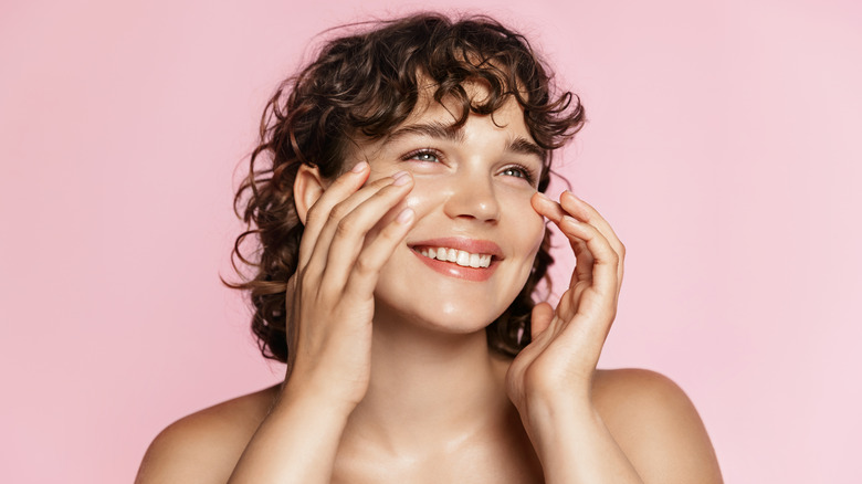 Woman smiles as she applies skincare to face