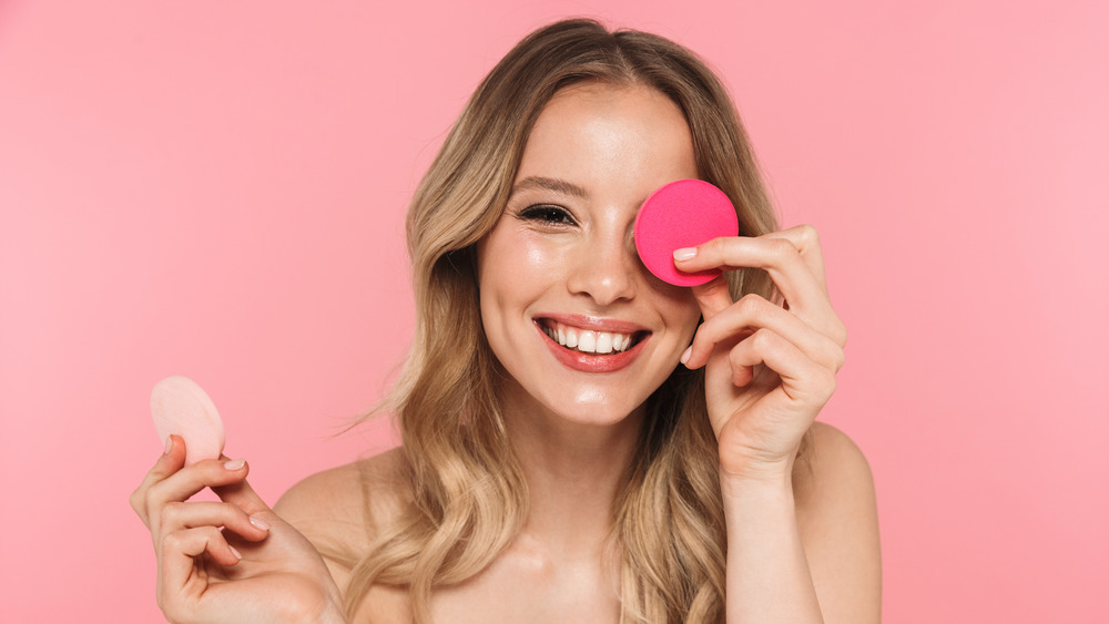 A smiling woman holding up beauty sponges 