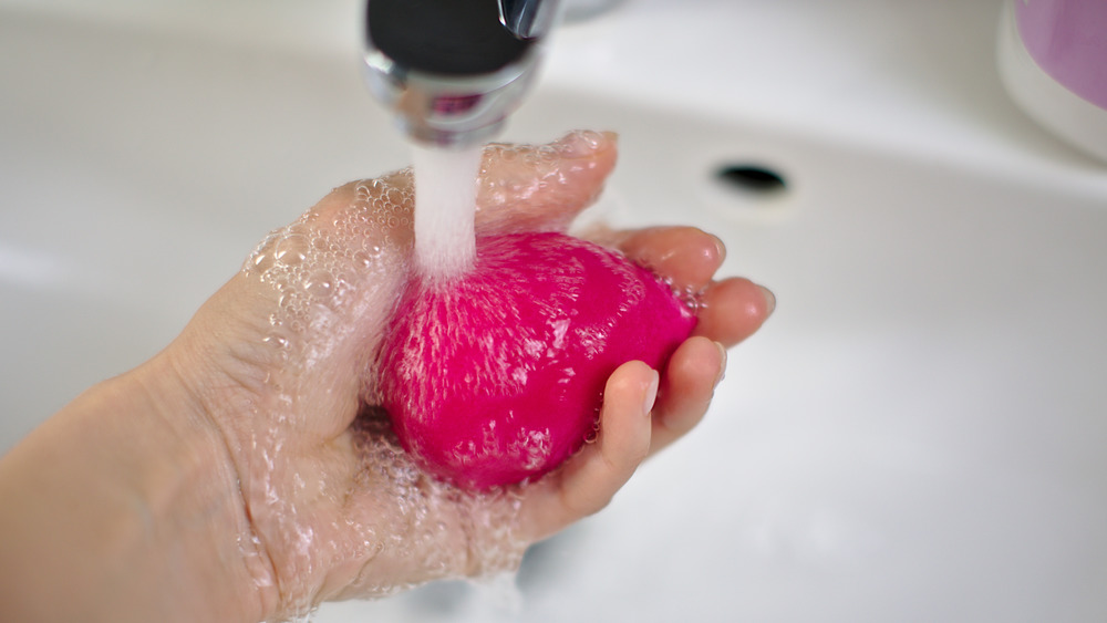 A Beauty Blender being held under a faucet 