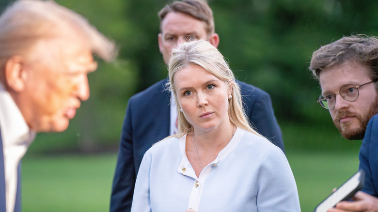 Press Secretary Karoline Leavitt stands and listens to President Donald Trump speaking