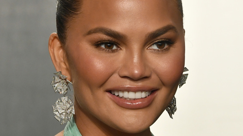 Chrissy Teigen smiling hair back and statement earrings