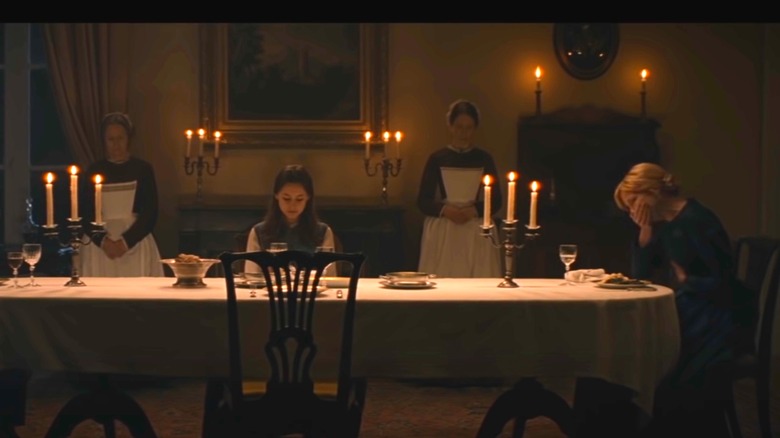 Kelly Reilly in black seated at table with hand over mouth in The Cursed