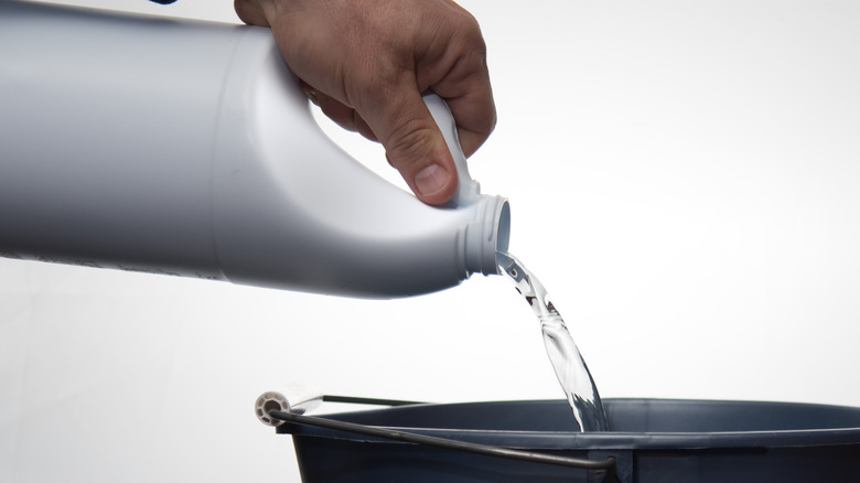 A hand pouring bleach into a bucket 