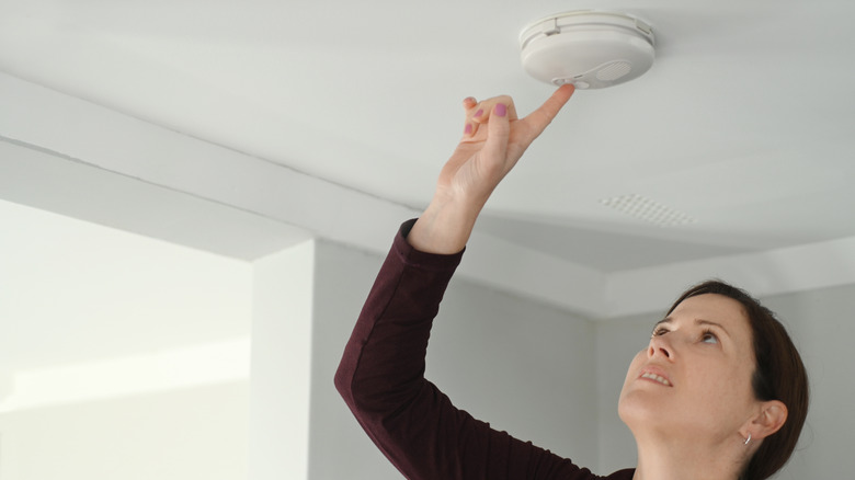 A woman pushing a button on a smoke detector 