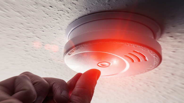 A hand pushing a button on a smoke detector 