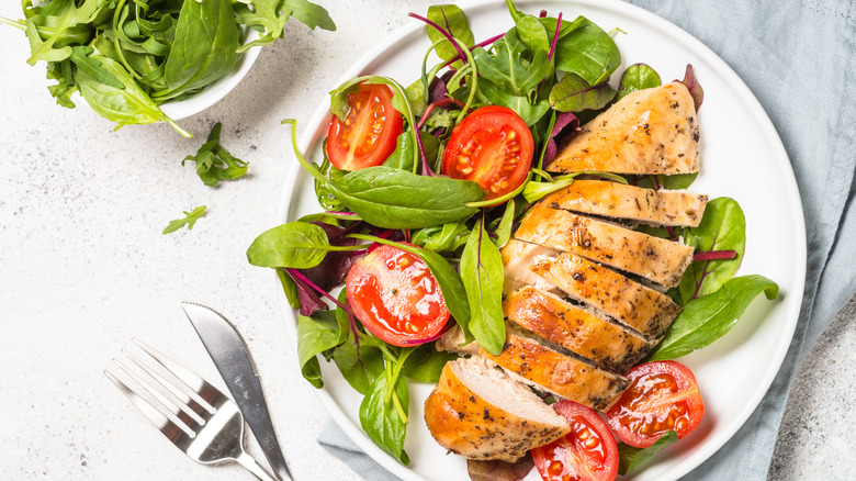 A plate of chicken and salad with an accompanying bowl of greens