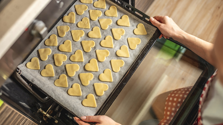 A cookie sheet covered with wax paper and heart shaped cookies 