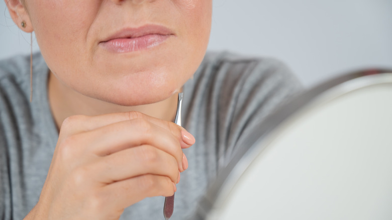 Woman using tweezers on her chin