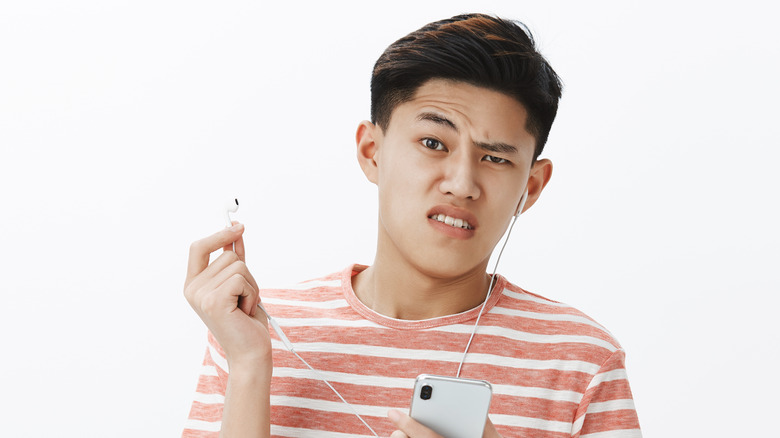 man holding broken earbud and raising eyebrow