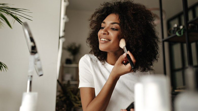 Young woman applying makeup to her face using a makeup brush