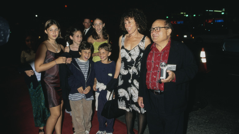 Danny DeVito holding a camera standing with Rhea Perlman and their children on the red carpet