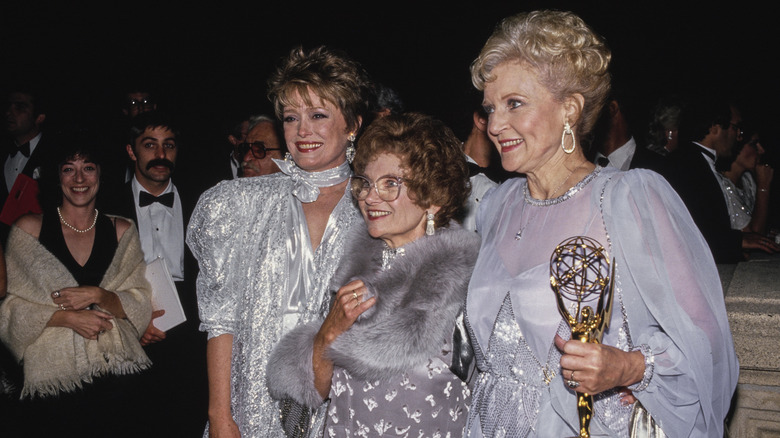 Rue McClanahan, Estelle Getty, and Betty White all smiling in silver or gray dresses at the 38th Primetime Emmy Awards in September 1986. White holds her Emmy for 'Outstanding Lead Actress in a Comedy Series'