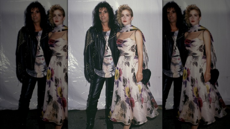 Alice Cooper wearing a leather outfit and posing next to Christina Applegate, who wears a white floral-print dress, at the 1989 MTV Video Music Awards.