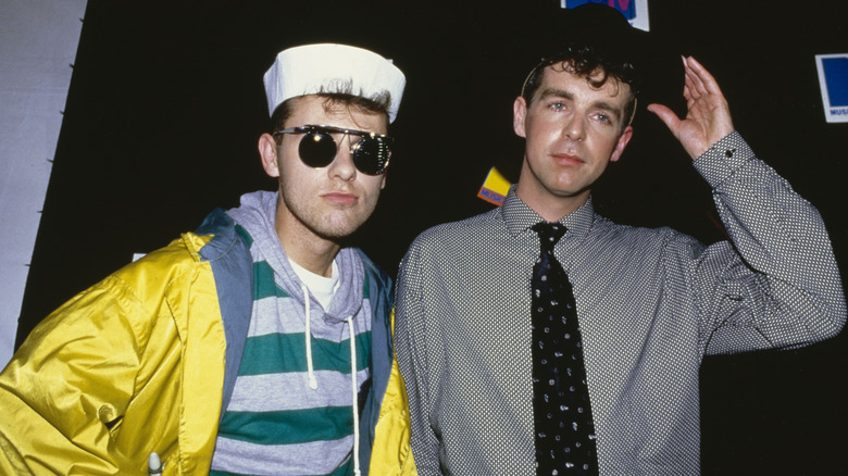 Chris Lowe wearing sunglasses and a sailor hat next to Neil Tennant, who wears a black brimmed hat and polka-dot tie, at the 1986 VMAs.