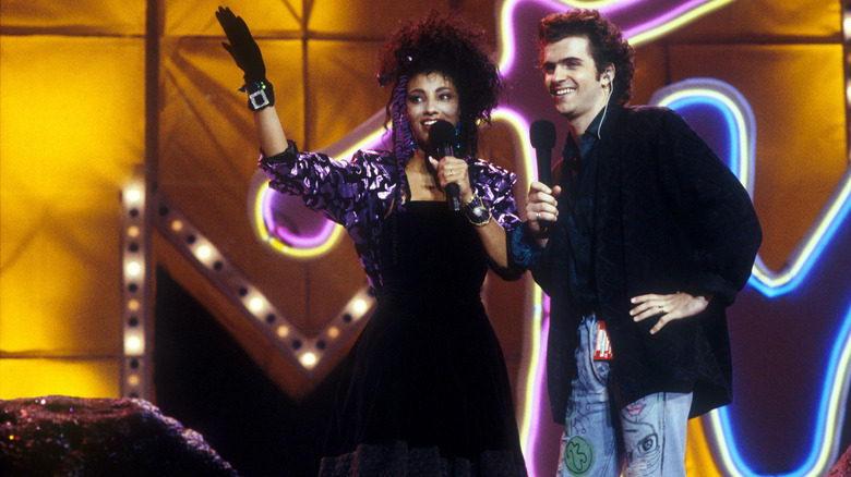 VJ Downtown Julie Brown holding up a gloved hand onstage beside Dweezil Zappa at the 1987 MTV VMAs.