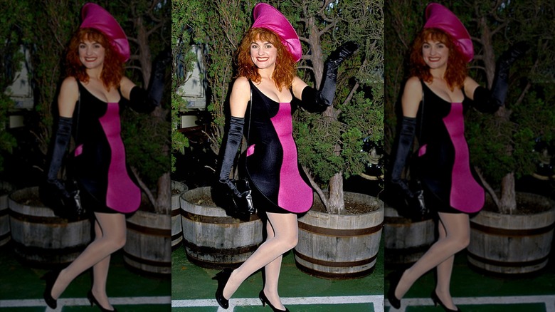 Julie Brown posing outdoors in a black and pink dress and matching hat shaped by hoops at the 1989 VMAs.
