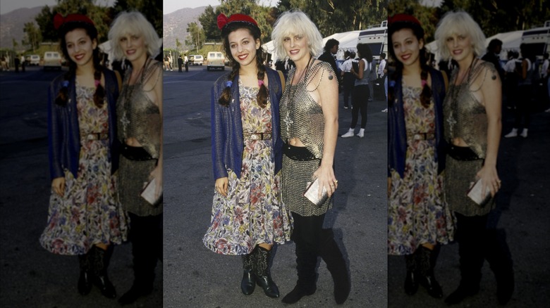 Moon Unit Zappa wearing a floral dress and cowboy boots and posing outdoors with Katie Wagner, who wears a chain-mail top and skirt, at the 1987 VMAs.