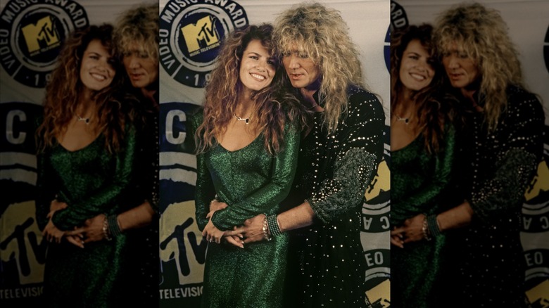 David Coverdale wearing a studded jacket and wrapping his arms around Tawny Kitaen, who wears a green sequined dress, at the 1987 MTV Video Music Video Awards.