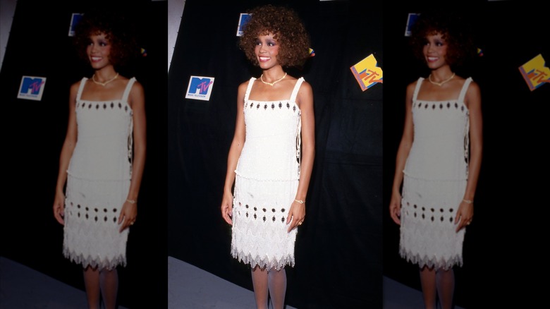 Whitney Houston smiling in a white top and matching fringe skirt at the 1986 MTV Video Music Awards.
