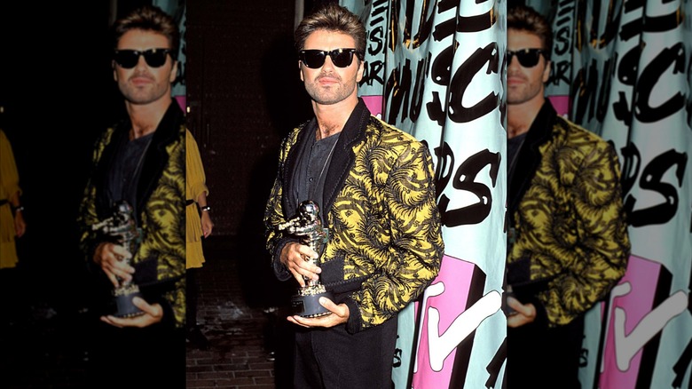 George Michael wearing a yellow jacket with a black organic pattern and holds his Vanguard Award at the 1989 VMAs.