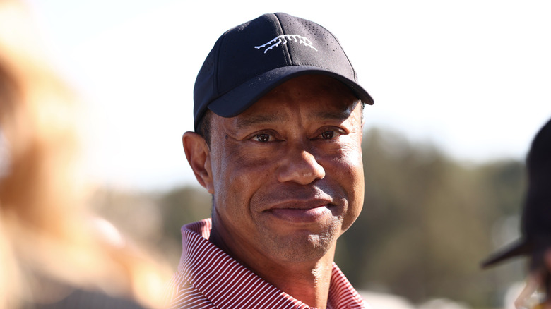 Tiger Woods smiling in a black hat and stripy red and white shirt