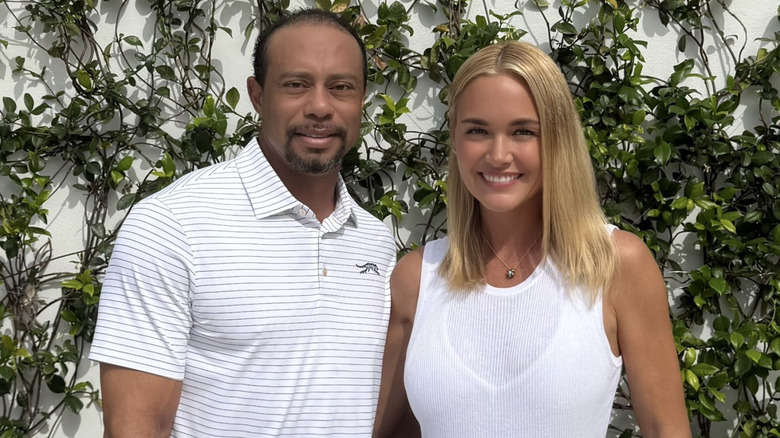 Tiger Woods and Vanessa Trump posing for a picture in front of a vine covered wall
