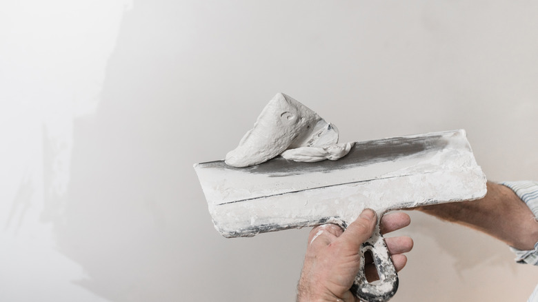 Construction worker with white mud on a spatula with drywall in the background.