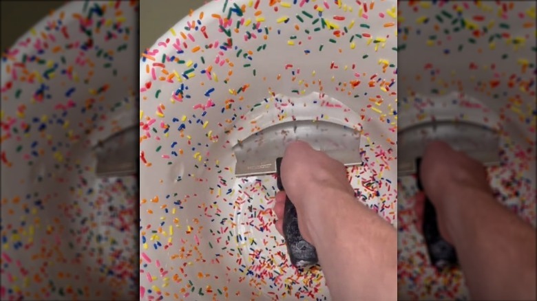 Man using a rounded scraper to scrape ice cream with sprinkles.