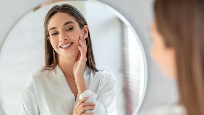 Woman touching her face while looking at herself in the mirror