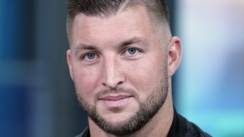 Tim Tebow gives a slight smile with a beard and mustache