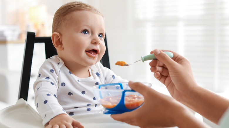 Baby in high chair about to take a bite of food from spoon