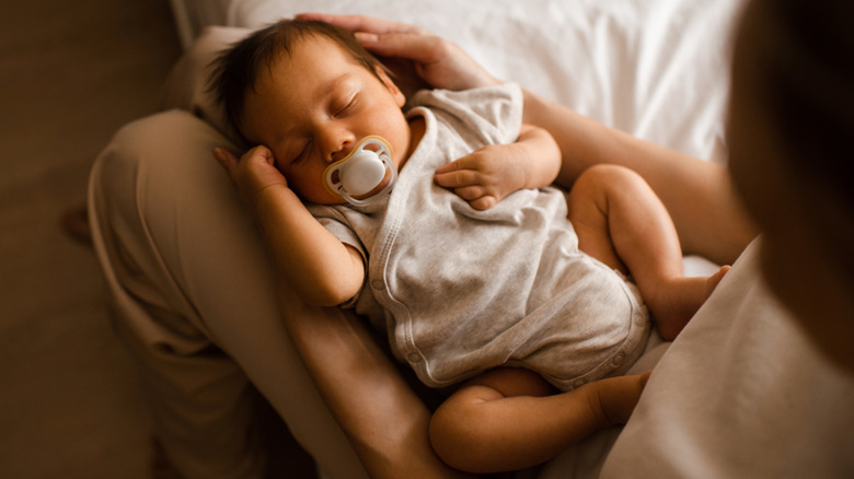 Baby with pacifier being held in adult's lap