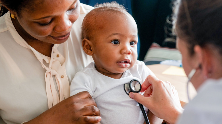 Baby being held by adult while doctor uses stethoscope