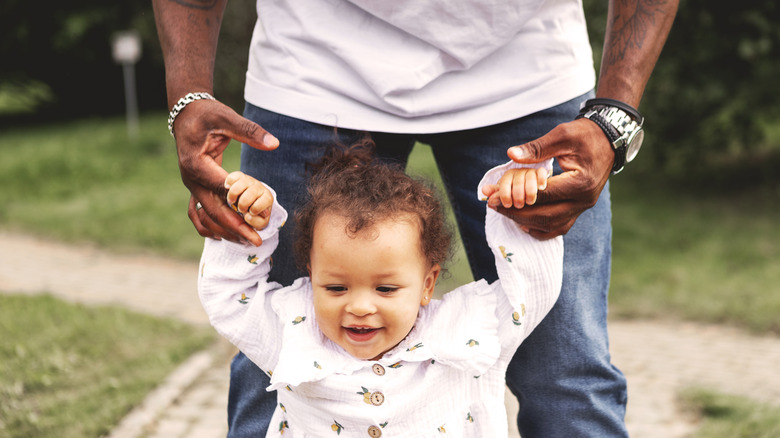 Baby walking and holding adult's hands