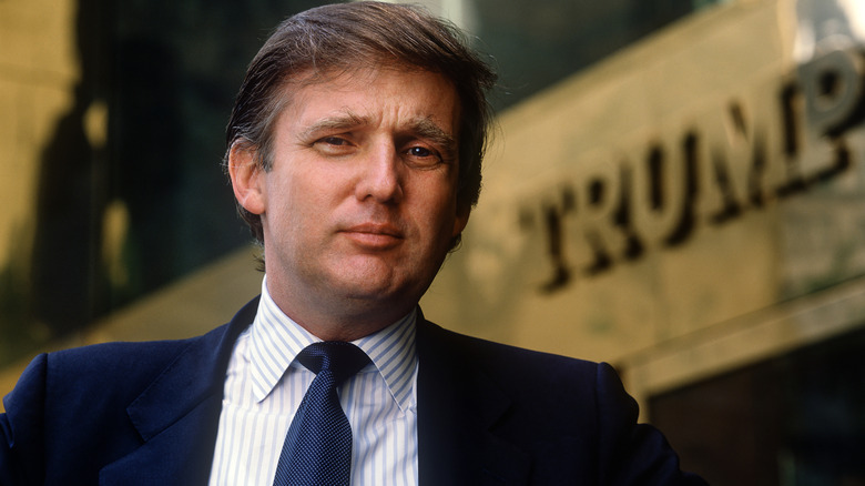 A younger Donald Trump posing in front of Trump Tower