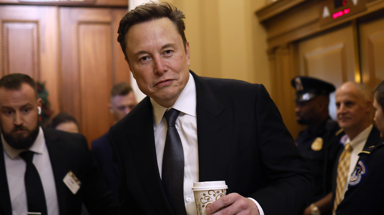 Elon Musk walking with a coffee cup in hand